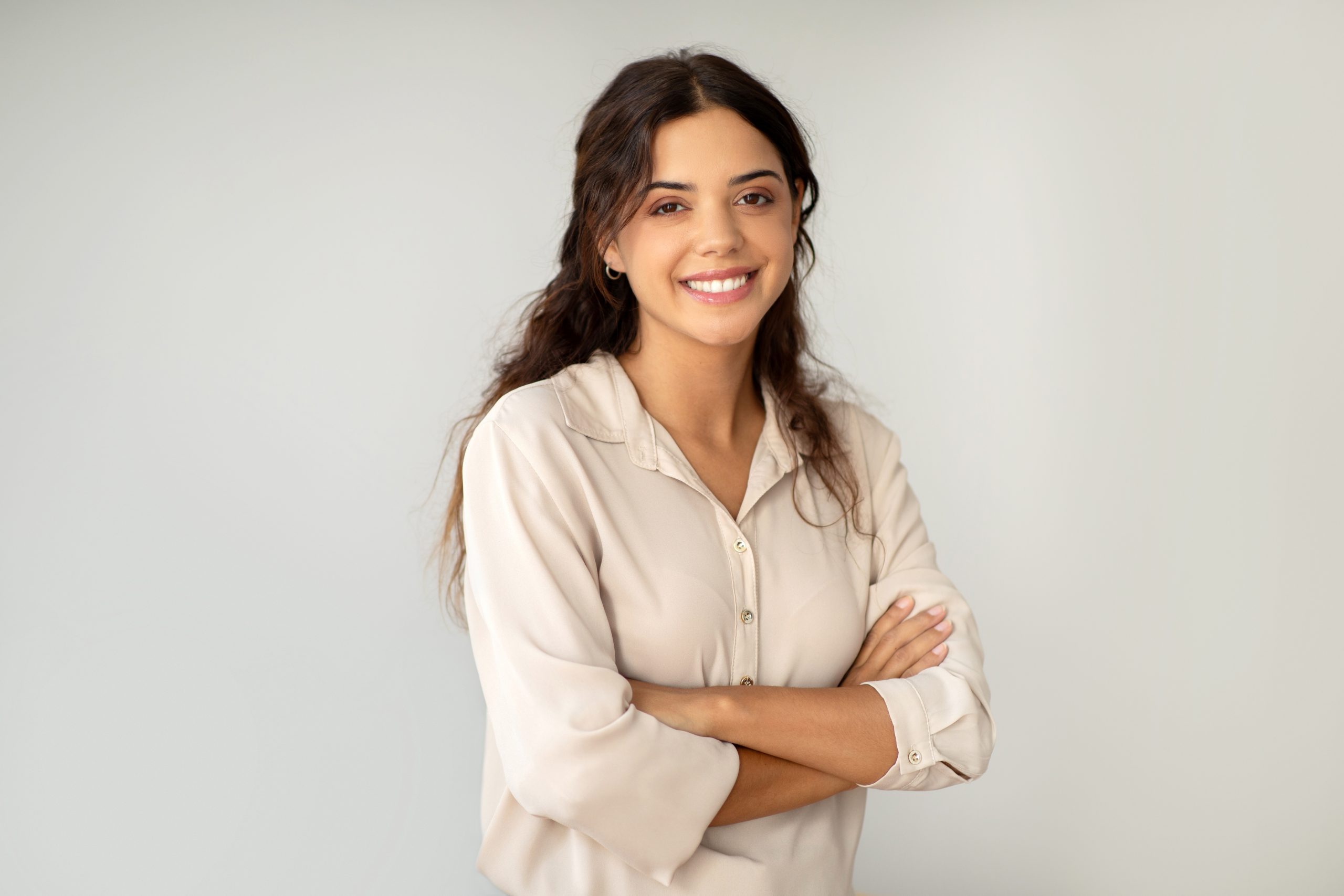 Smiling,Young,Woman,Standing,Confidently,With,Arms,Crossed,Over,Light